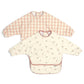 Pair of long-sleeve baby bibs: cream floral print and pink gingham bibs.