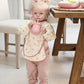 Long-sleeve baby bib in cream with tiny animal print and pink trim, worn by baby.