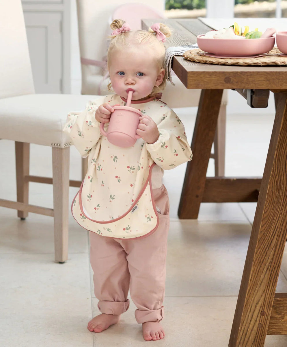 Long-sleeve baby bib in cream with tiny animal print and pink trim, worn by baby.