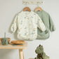 Two long-sleeve baby bibs: cream dinosaur print and sage green bib set.