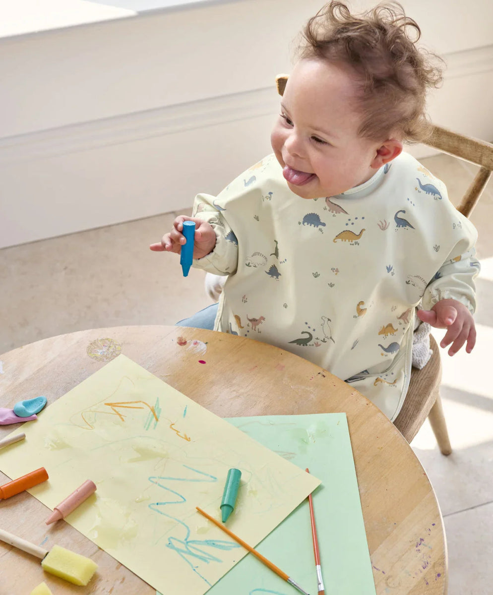 Long-sleeve baby bib in cream with blue animal print, worn by a smiling child.