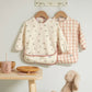 Two long-sleeve baby bibs: cream floral print and blush check style bibs.