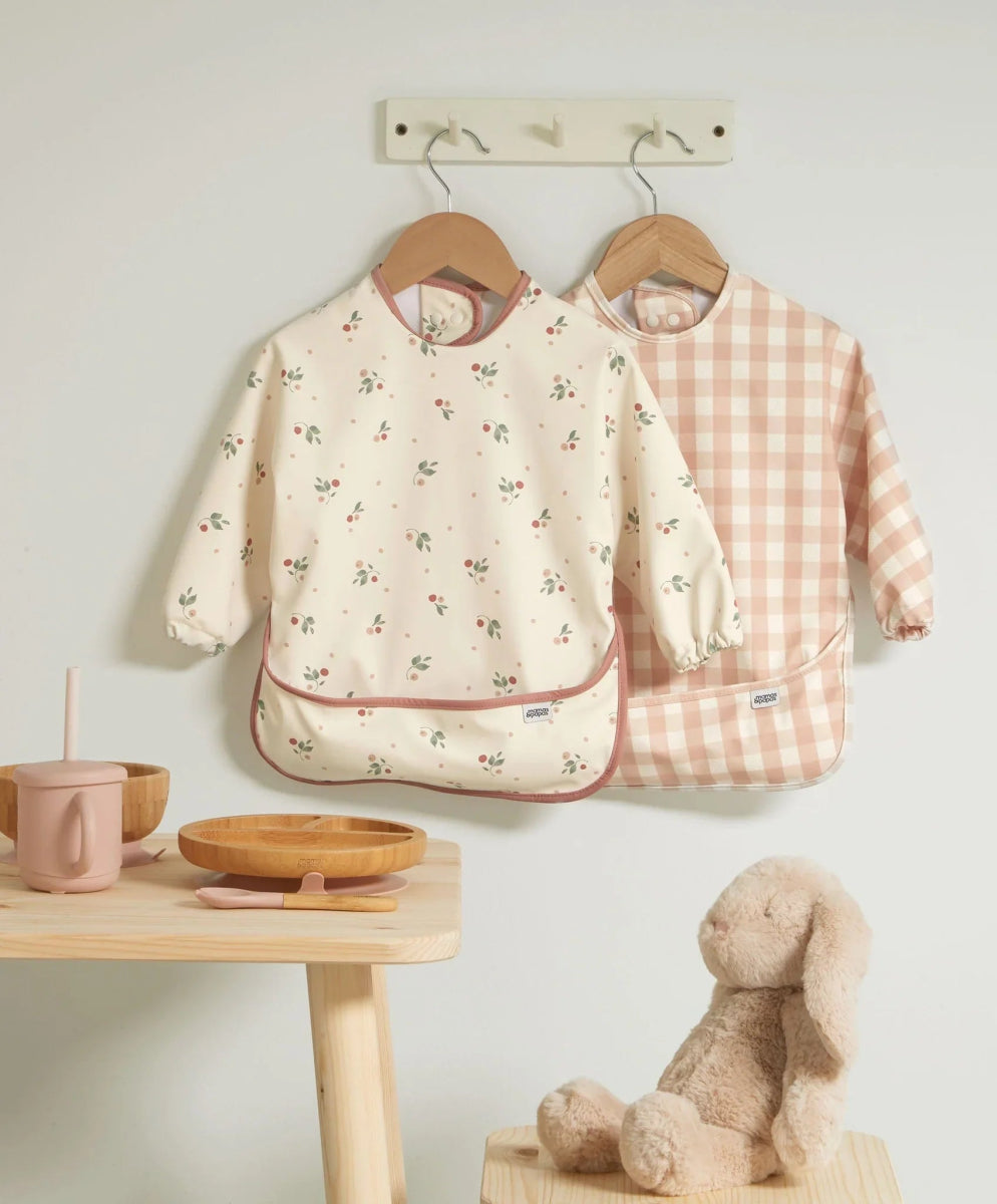 Two long-sleeve baby bibs: cream floral print and blush check style bibs.
