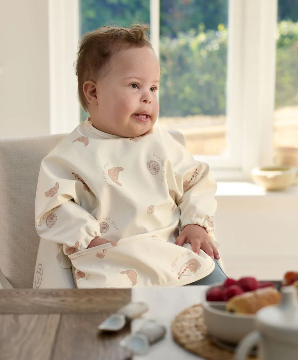 Long-sleeve baby bib in cream with small animal prints, worn by a child.