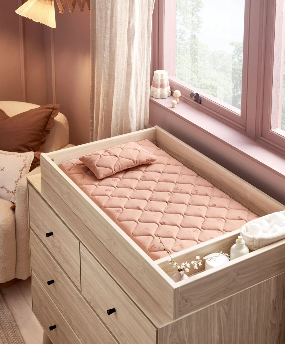 Quilted blush changing pad with wildflower print in a light wood drawer frame