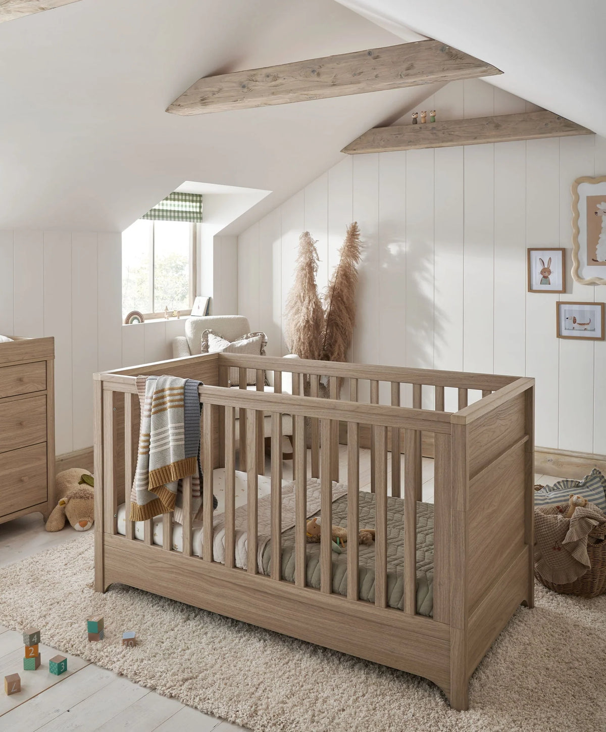 Oak cot bed with vertical slats and fitted bedding