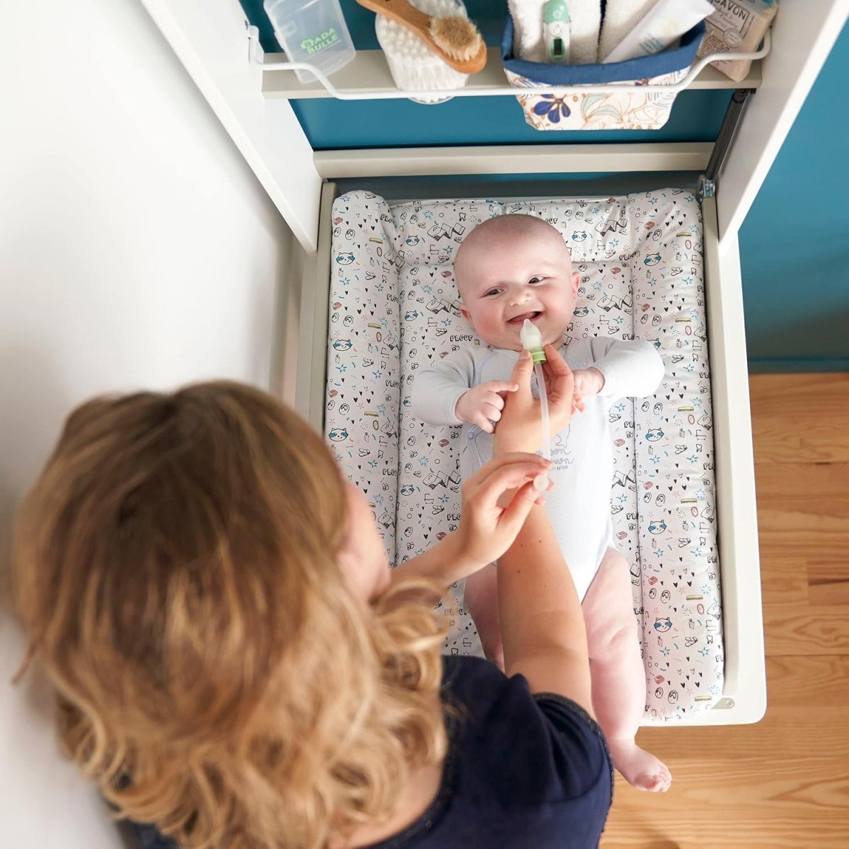 Caregiver holds nasal aspirator tip at baby’s nose in open drawer