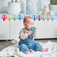 Baby holding a teal monkey teether with ring handles and smiling face