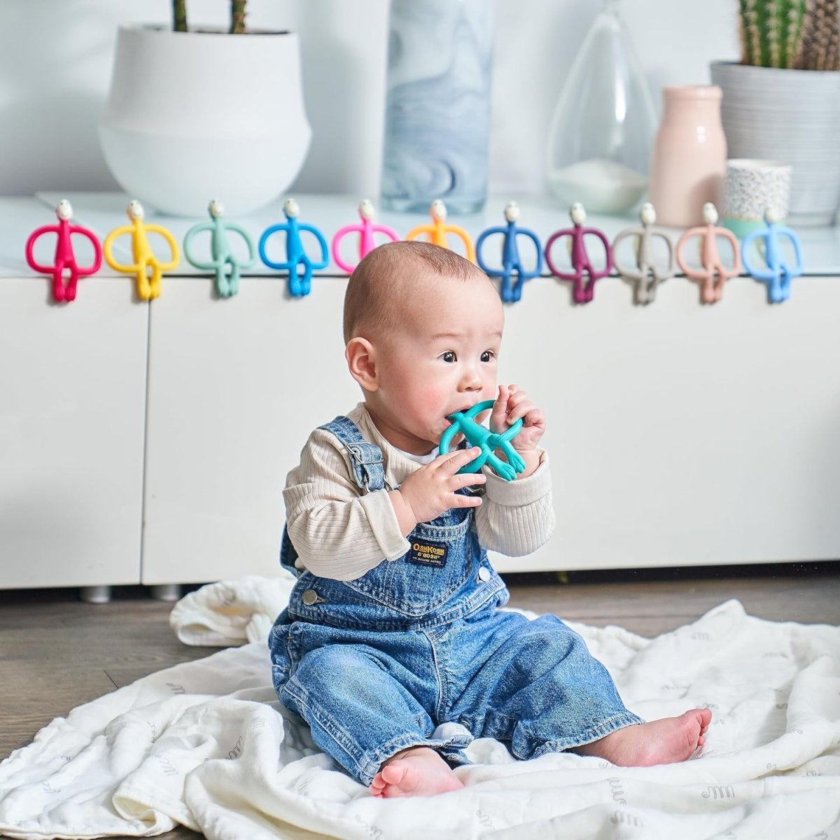 Baby holding a teal monkey teether with ring handles and smiling face