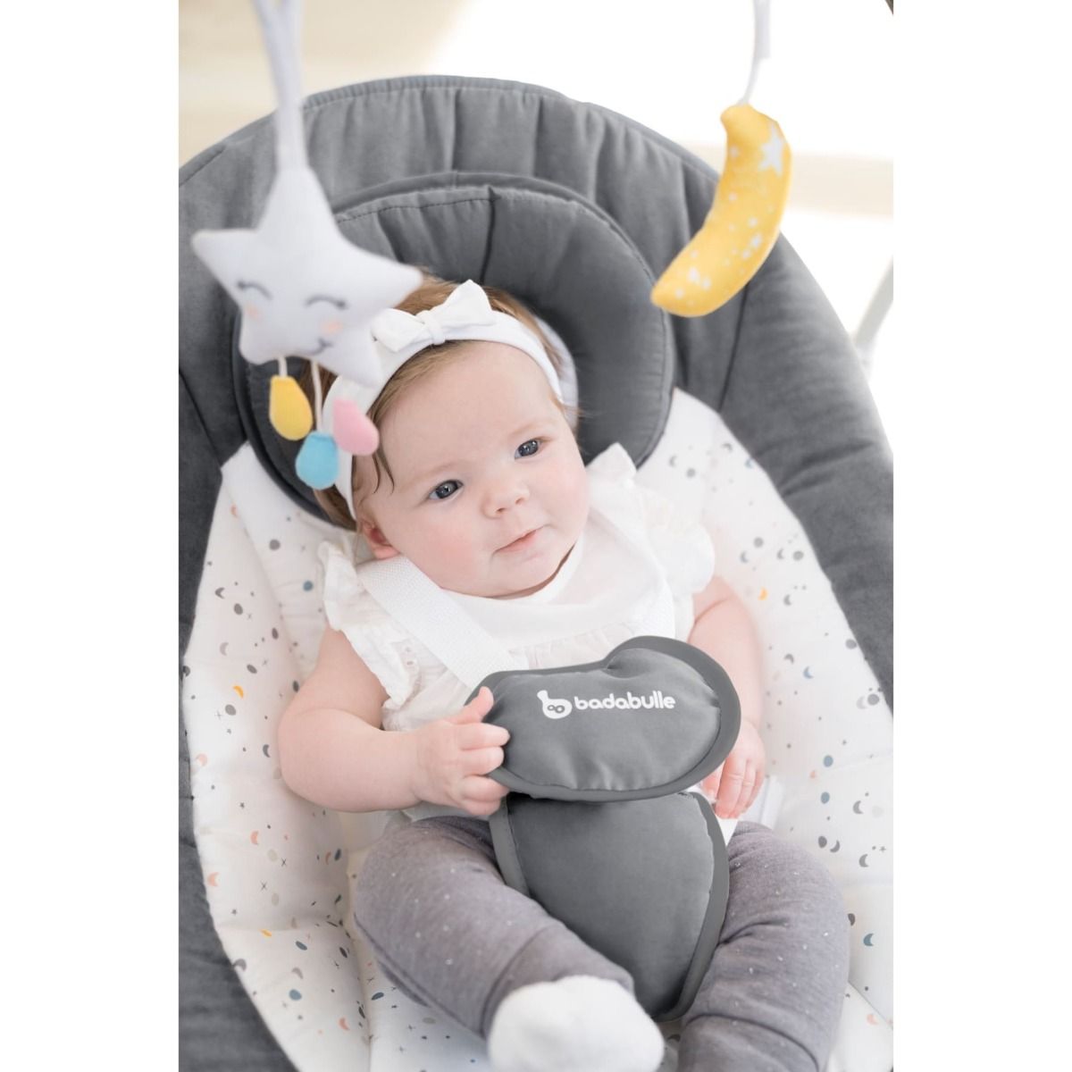 Baby in infant swing with gray seat and hanging moon, star, and bell toys