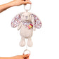 Plush rabbit baby toy keychain held up, with floral wing print and fabric ribbon tag