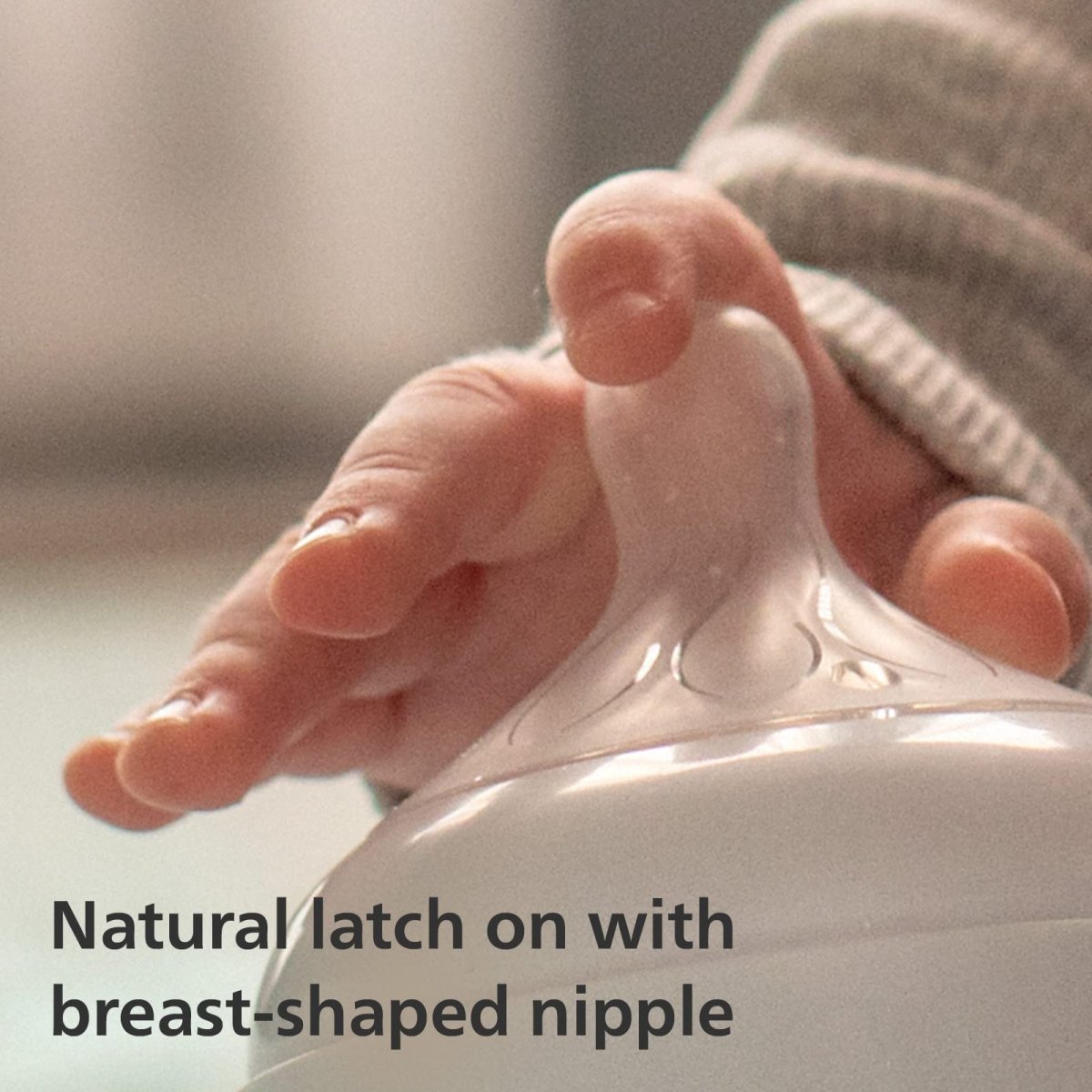 Baby bottle nipple with breast-shaped tip, clear bottle held by fingers