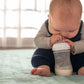 Baby holding a clear feeding bottle with white teat
