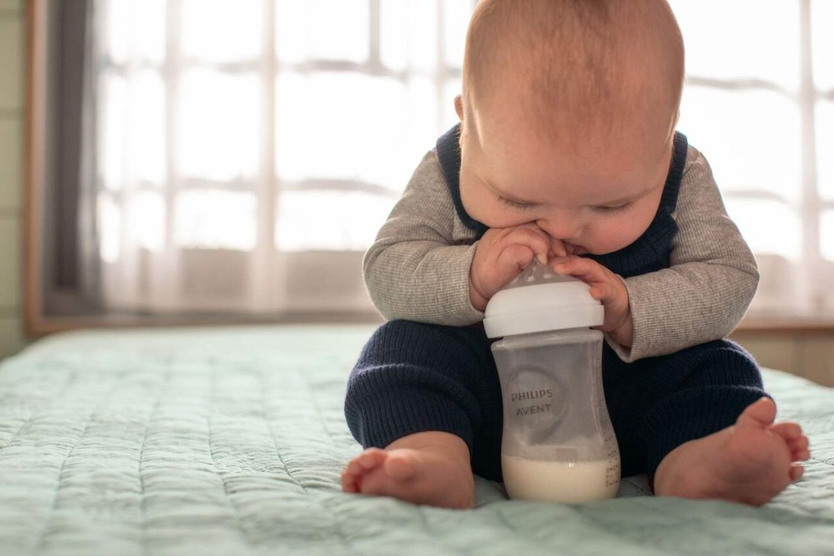 Baby holding a clear feeding bottle with white teat