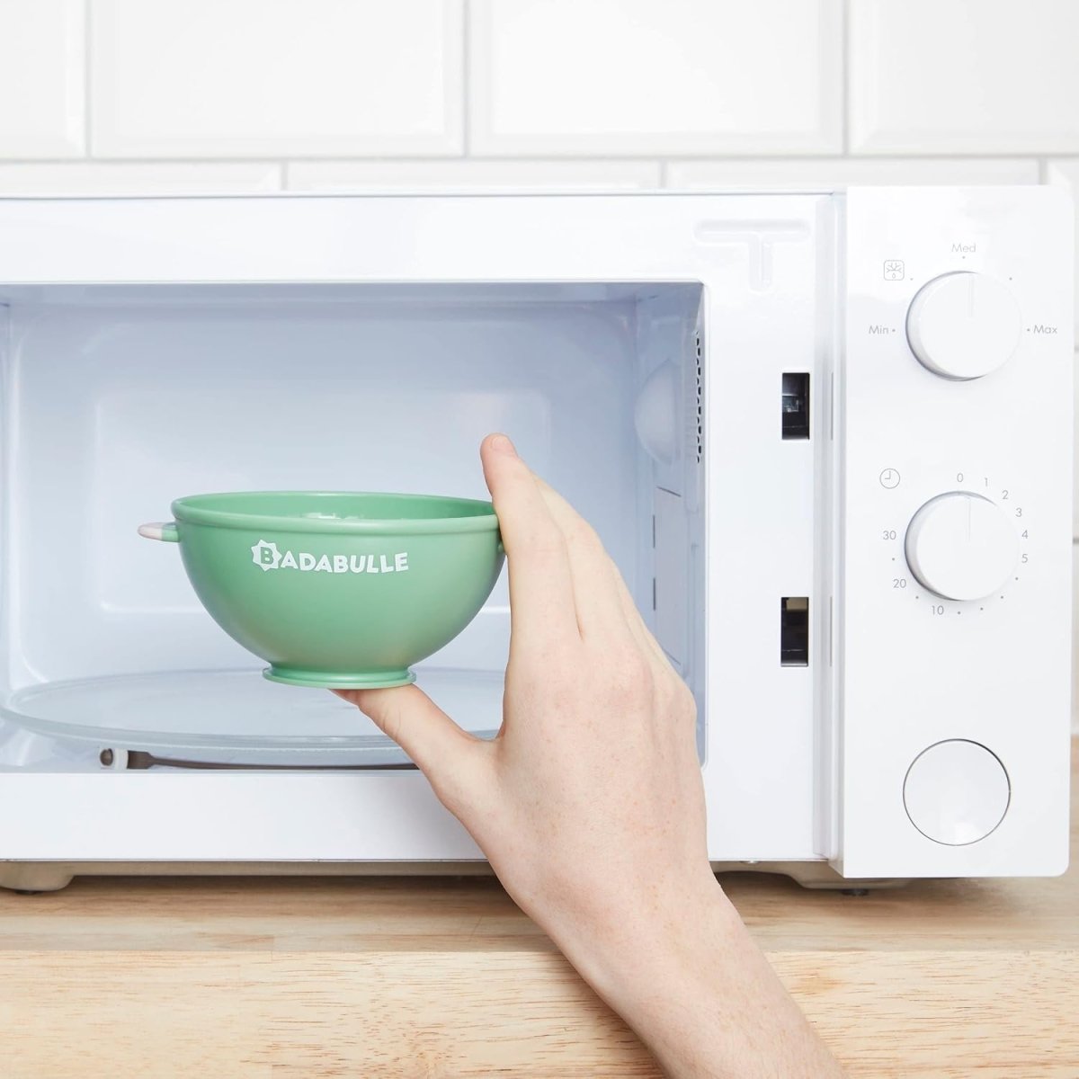 Green non-slip bowl inside microwave, hand placing bowl on tray