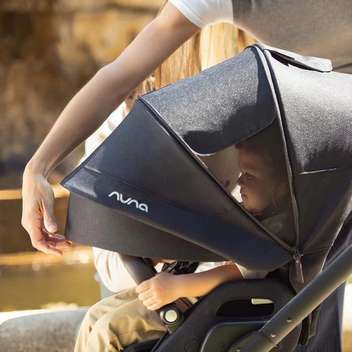 Black infant car seat with canopy raised, carry handle and Nuna logo visible.