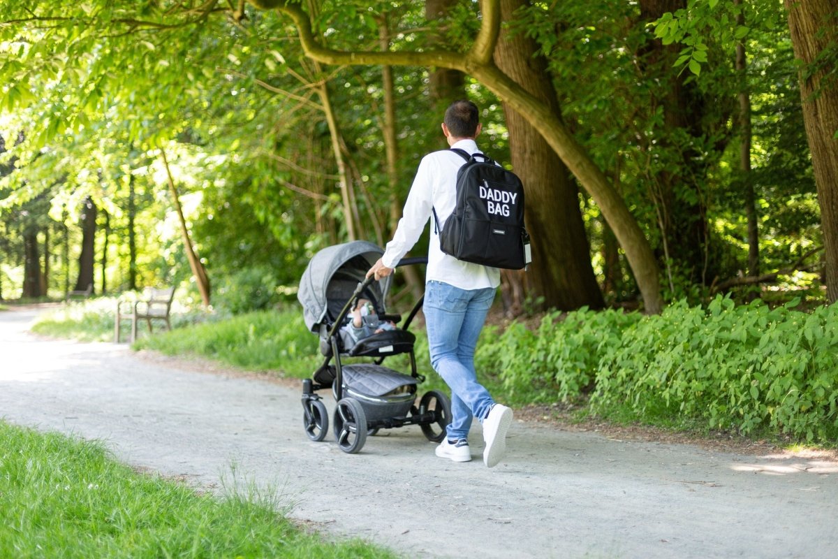 Nursery backpack on adult pushing stroller, dark 'DADDY BAG' print on back
