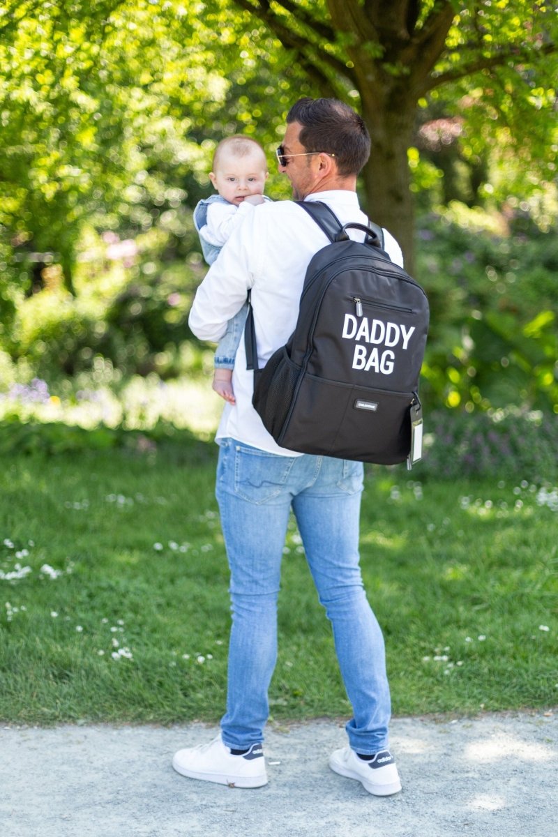 Nursery backpack on parent with 'DADDY BAG' print while holding baby