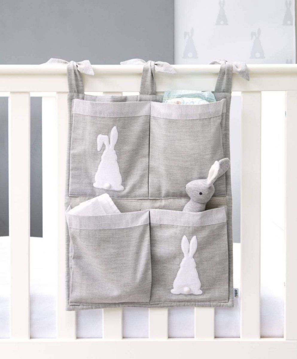 Grey hanging nursery organizer with four pockets and bunny appliques, on a crib rail