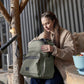 Olive green backpack with front zip pocket and side compartments, worn on back
