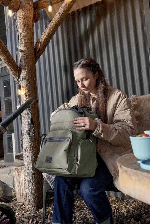 Olive green backpack with front zip pocket and side compartments, worn on back