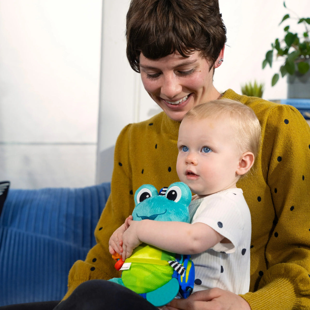 Turquoise frog activity plush toy with ring handle, held by a baby