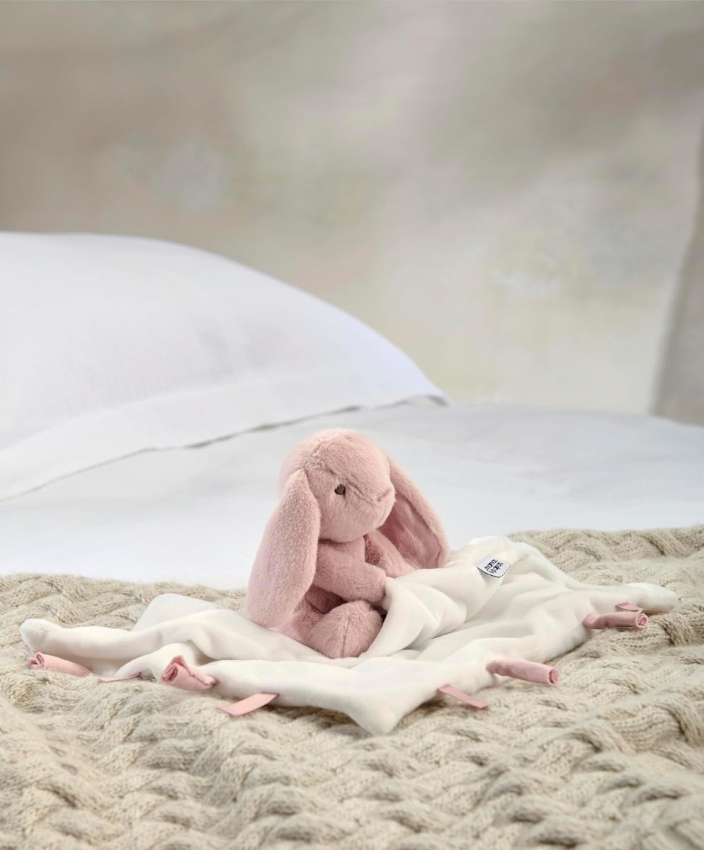 Pink bunny comforter with small plush bunny on folded white blanket with pink accents
