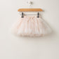 Light pink tulle tutu skirt hanging on wooden hanger with clips