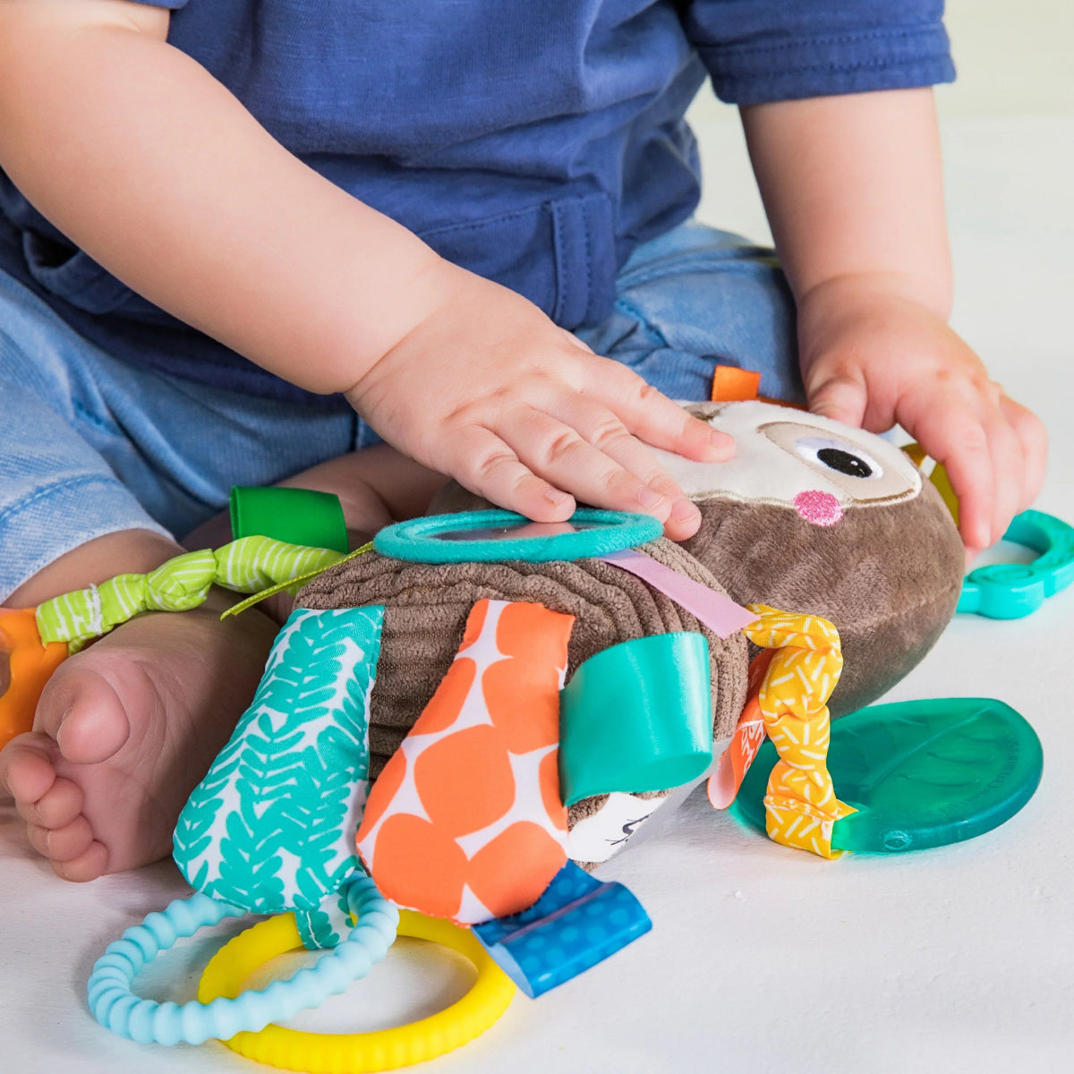 Plush activity toy with teal spine, orange patterned panel, and crinkly dangling straps.