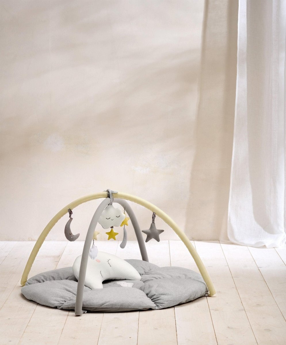 Round beige playmat with arched frame, hanging star and moon toys over cushioned pad