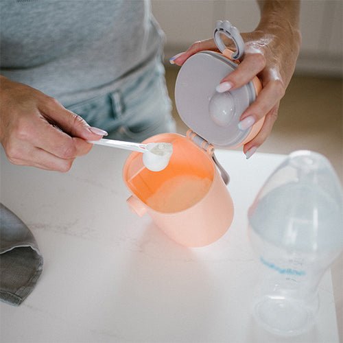 Milk powder dispenser pouring scoop into bottle, white plastic scoop and cap visible