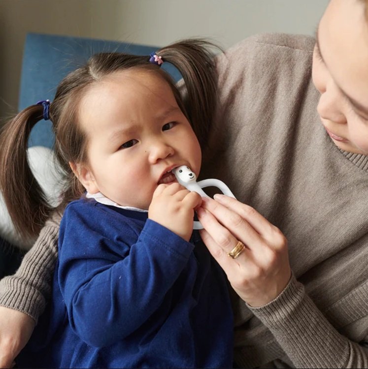 Baby using a bear-shaped teething ring held near her mouth