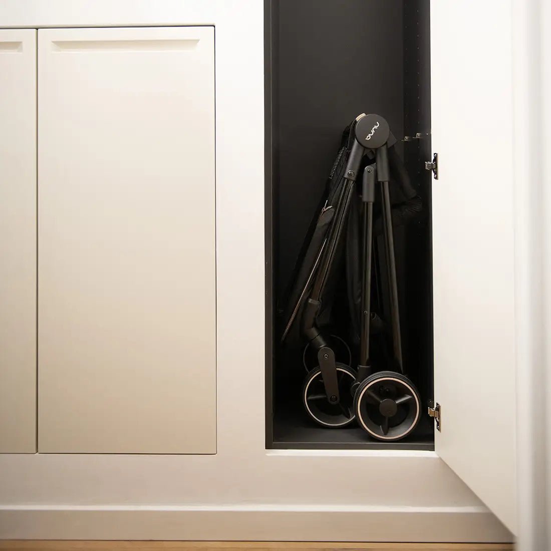 Folded black pushchair with canopy and wheels positioned by an open doorway