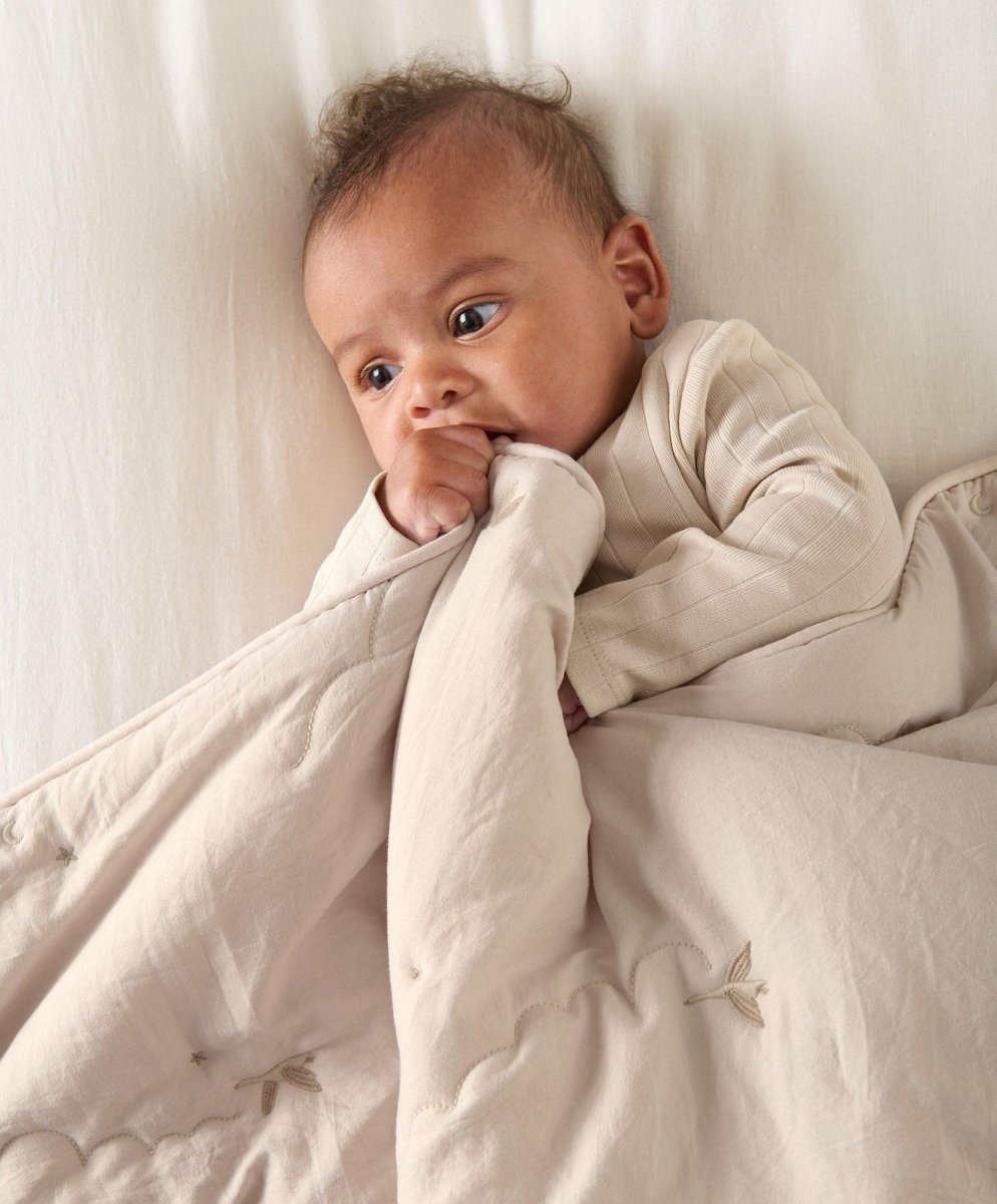 Soft taupe quilt with stitched motifs, draped over an infant