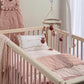 Light pink quilt draped on a baby crib mattress edge, with diamond stitching and floral motifs