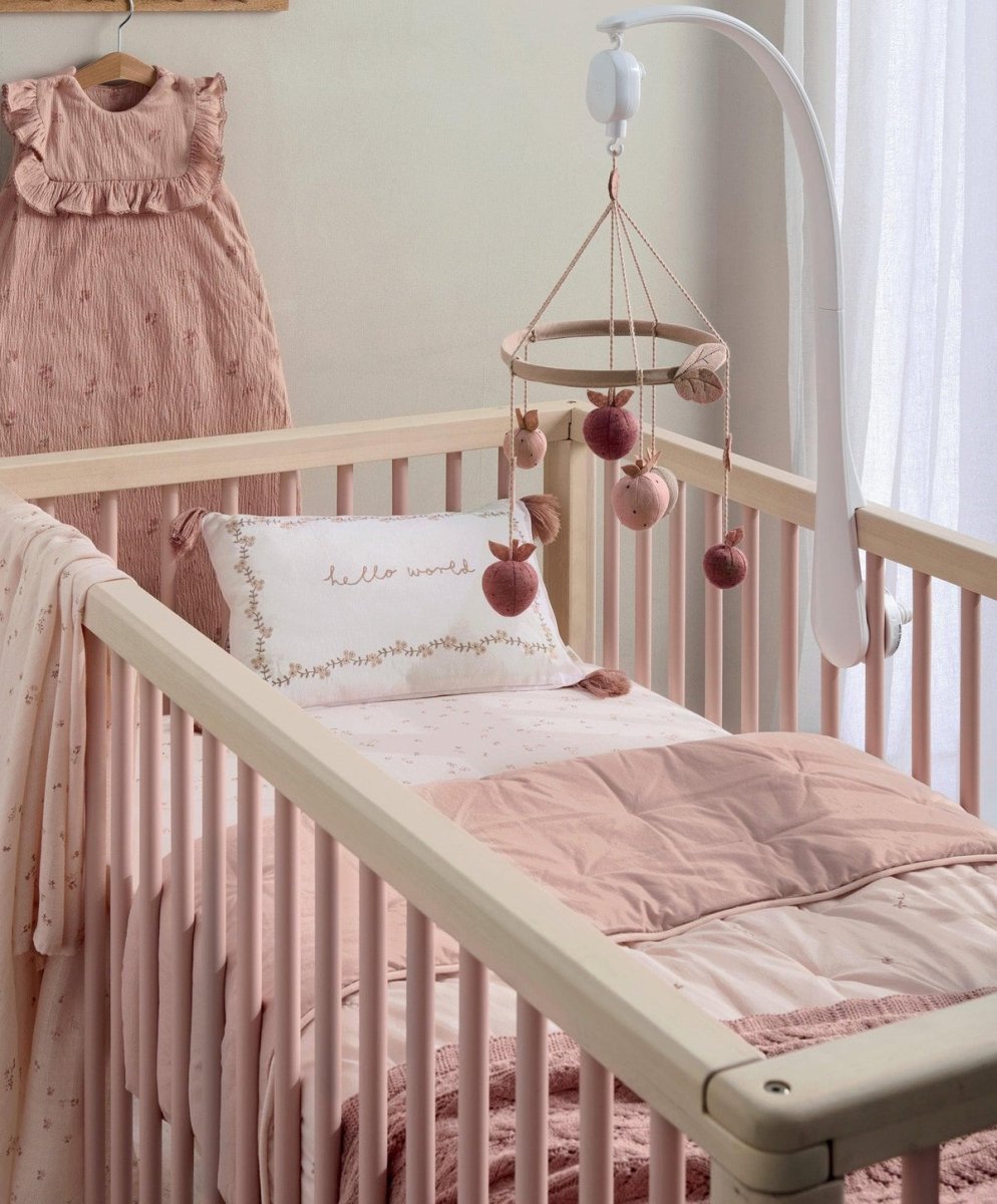 Light pink quilt draped on a baby crib mattress edge, with diamond stitching and floral motifs