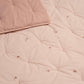 Close-up of light pink quilt showing diamond quilting and tiny embroidered floral motifs