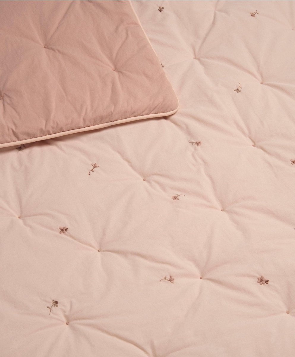 Close-up of light pink quilt showing diamond quilting and tiny embroidered floral motifs