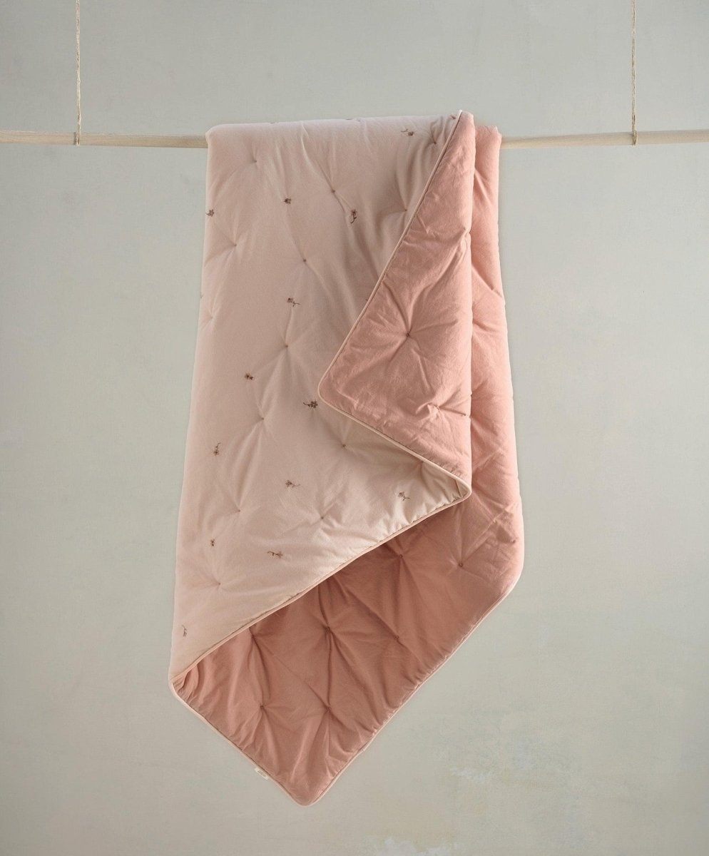 Light pink baby quilt with diamond stitching and small embroidered wildflower motifs