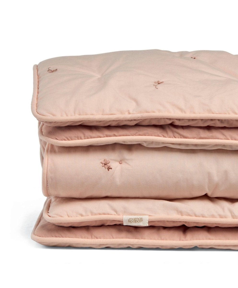 Folded light pink quilt with embroidered small floral details on quilted surface