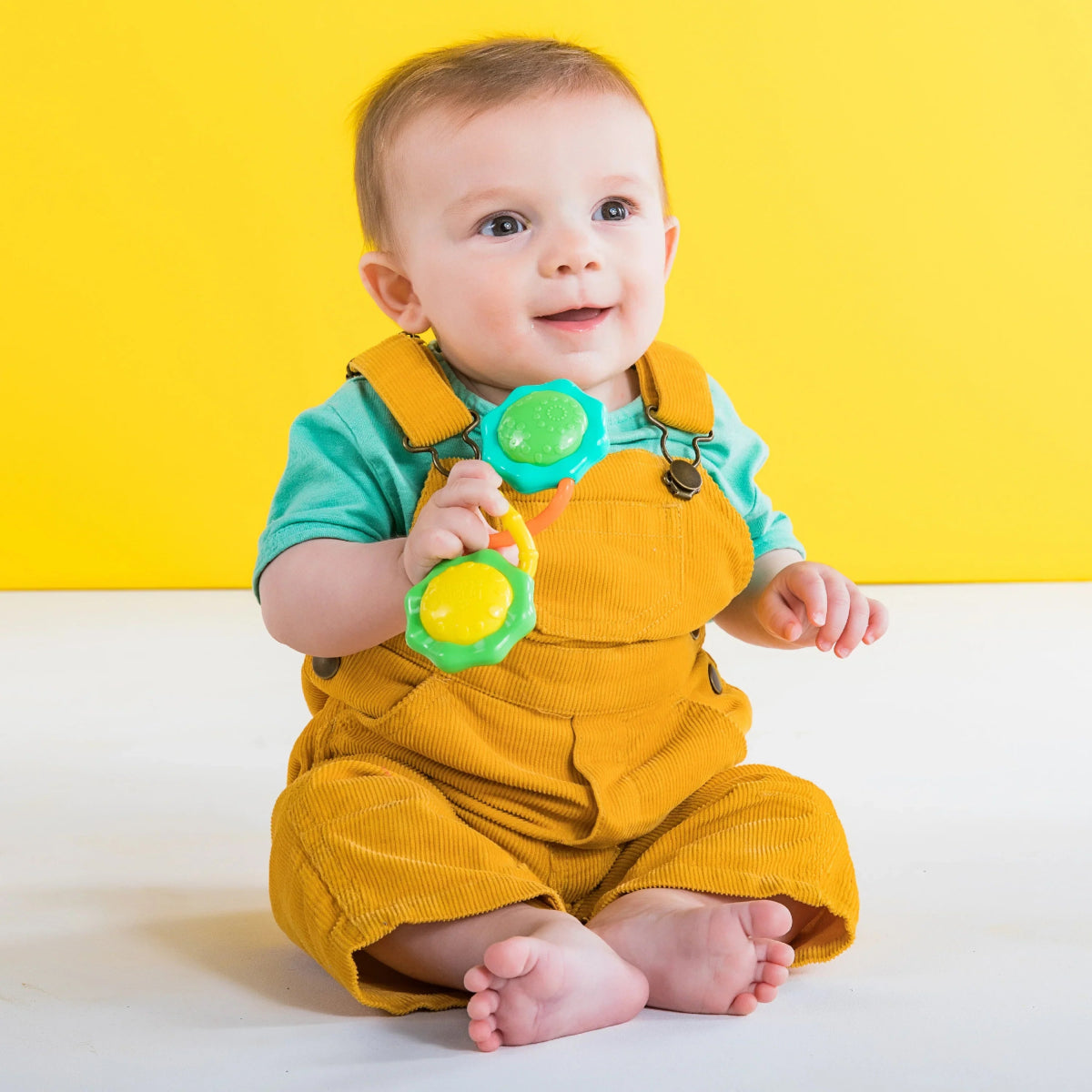 Barbell rattle toy with green and yellow end discs, baby holding the handle