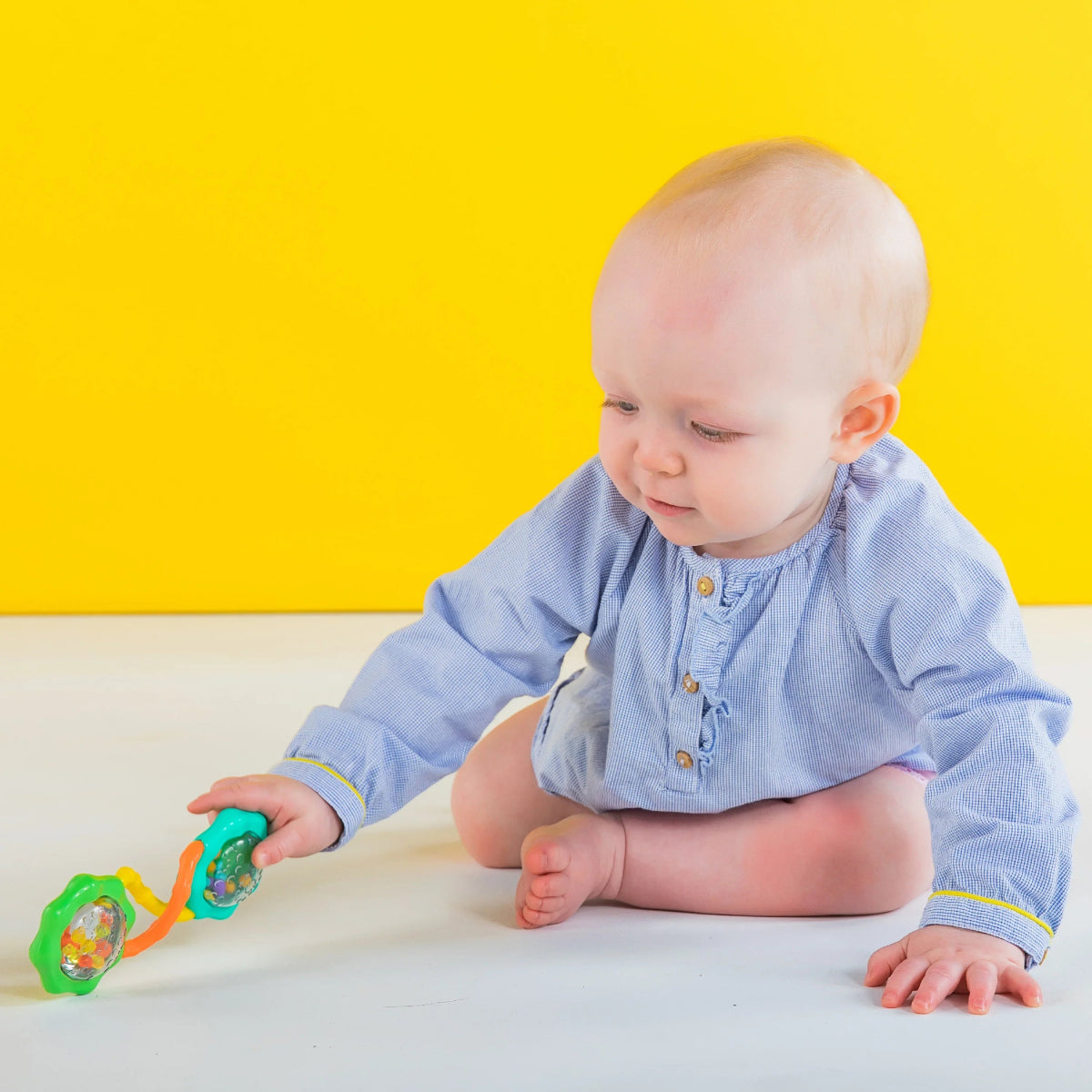 Barbell rattle toy with green end discs and orange/yellow handle, held by baby