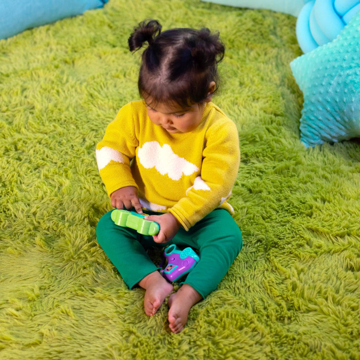 Toddler playing with teal safari driver toy car on a green shag rug