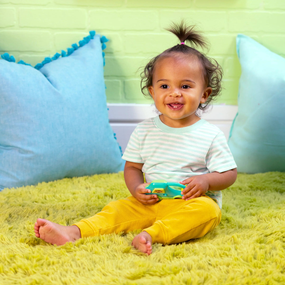 Toy safari driver car in hands, held by a smiling toddler on a rug