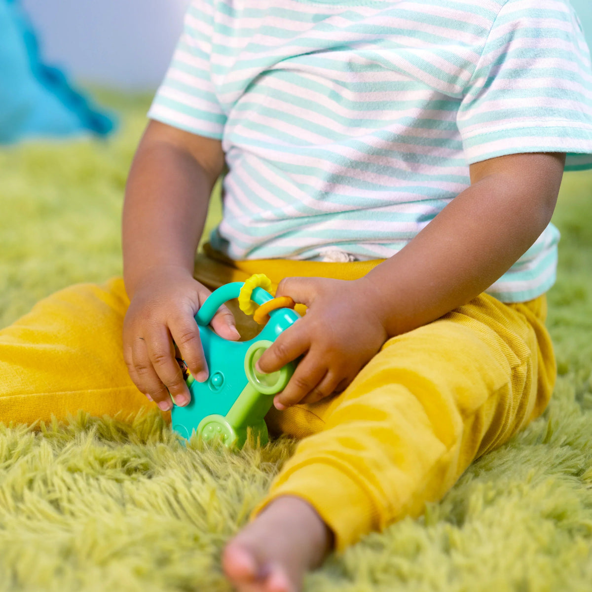 Toddler hands holding teal safari driver toy car on a green shag rug