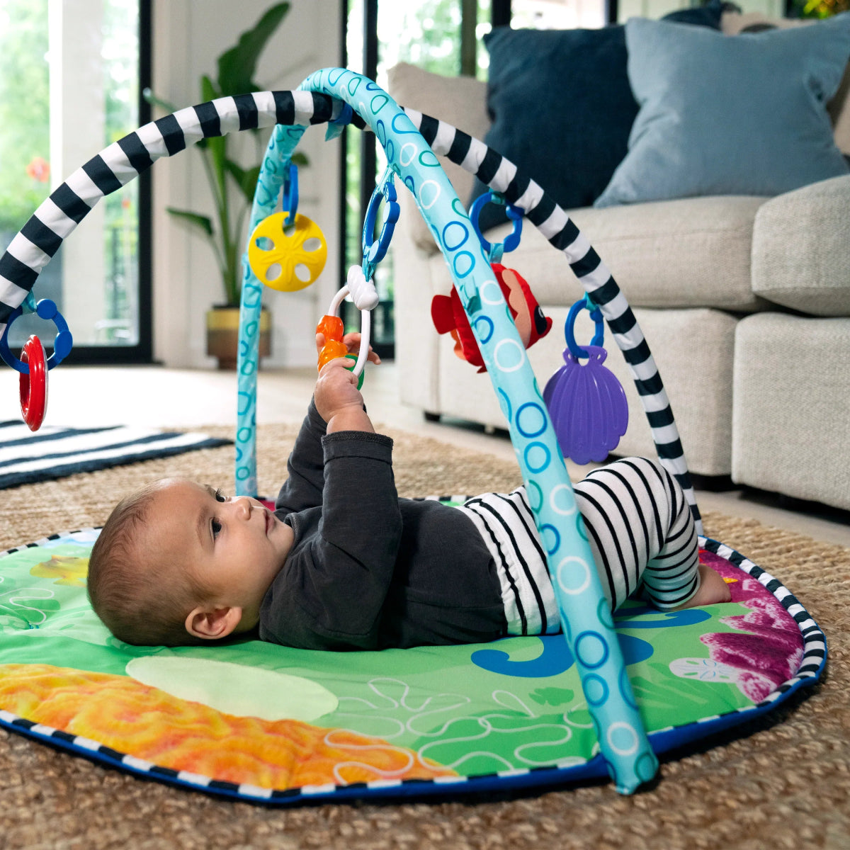 Water mat play gym with arch toys and infant lying on ocean-themed mat