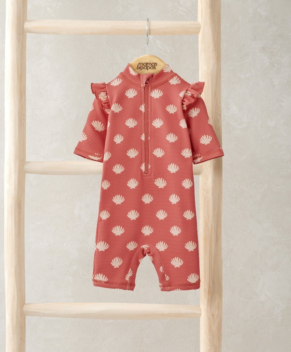 Coral pink rashsuit with all-over white shell pattern, zip front and ruffle sleeves.