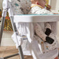 Baby high chair with white tray and animal-print seat, baby sitting with back facing