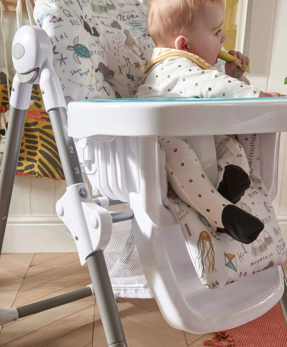 Baby high chair with white tray and animal-print seat, baby sitting with back facing