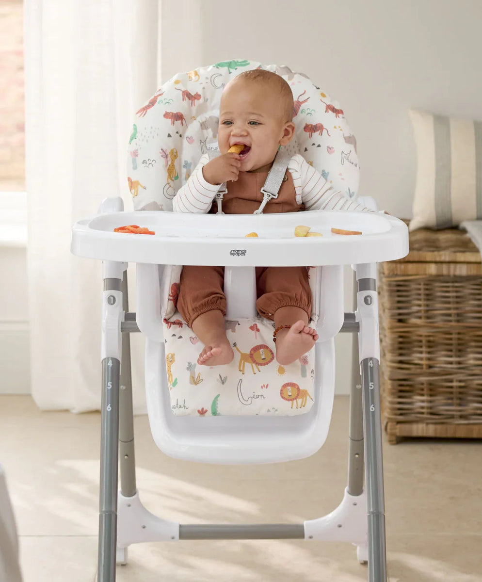 Baby high chair with white tray and animal-print cushion holding a seated baby